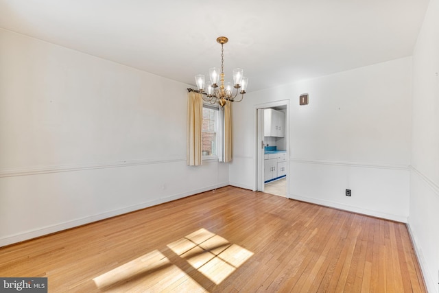 unfurnished room featuring light wood-style floors, a chandelier, and baseboards