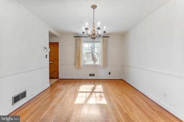 unfurnished dining area featuring visible vents, a chandelier, and wood finished floors