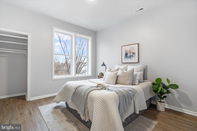 bedroom with a closet, visible vents, baseboards, and wood finished floors