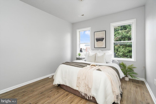 bedroom with multiple windows, visible vents, baseboards, and wood finished floors