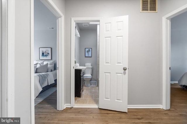 corridor with baseboards, visible vents, and wood finished floors