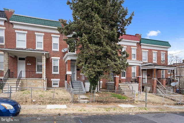 townhome / multi-family property featuring a fenced front yard, a tile roof, brick siding, and mansard roof