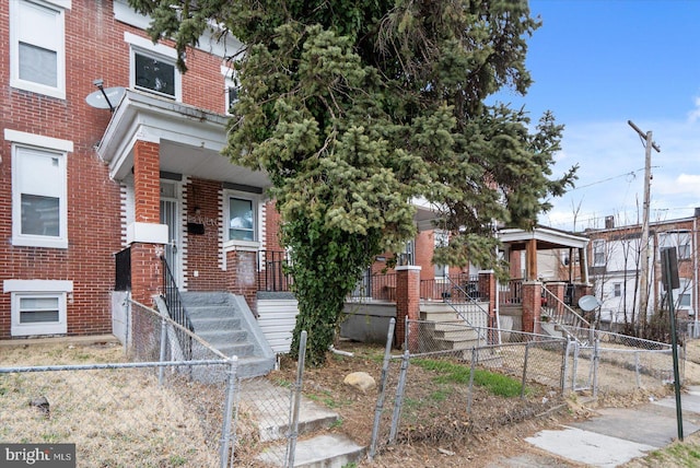 view of front of house with a fenced front yard, brick siding, a porch, and stairway