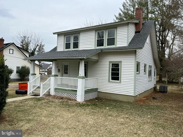 view of front facade with covered porch, central AC, a shingled roof, a front lawn, and a chimney