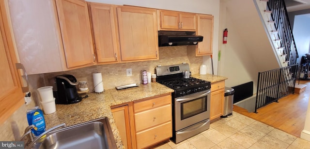 kitchen featuring light stone counters, tasteful backsplash, stainless steel range with gas stovetop, a sink, and under cabinet range hood