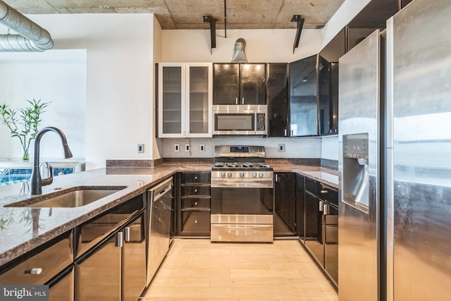 kitchen with light wood-style flooring, stainless steel appliances, a sink, backsplash, and dark stone countertops