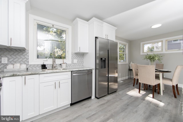 kitchen with light stone counters, stainless steel appliances, light wood-style floors, white cabinetry, and a sink