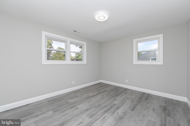 spare room featuring light wood-type flooring, plenty of natural light, baseboards, and visible vents