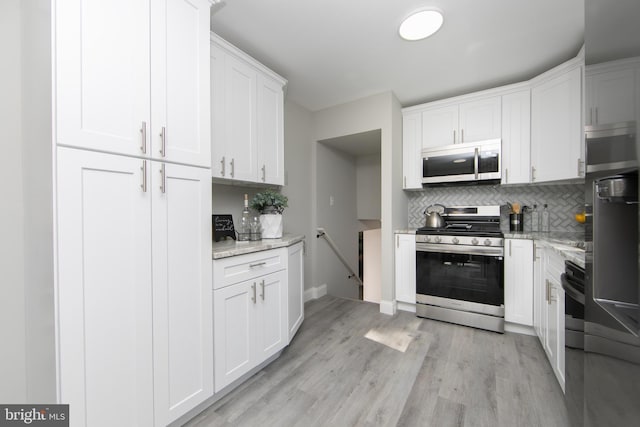 kitchen featuring white cabinets, light stone countertops, stainless steel appliances, and backsplash