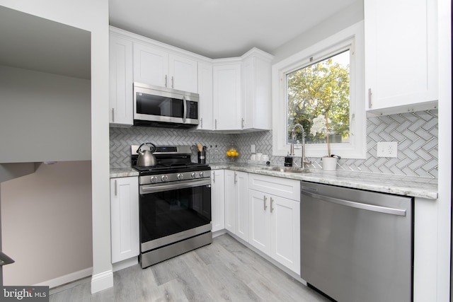 kitchen featuring appliances with stainless steel finishes, white cabinets, a sink, and light stone countertops