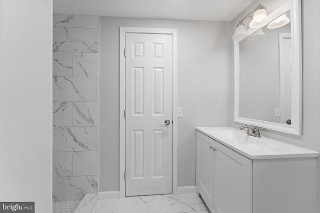 bathroom with marble finish floor, a tile shower, vanity, and baseboards