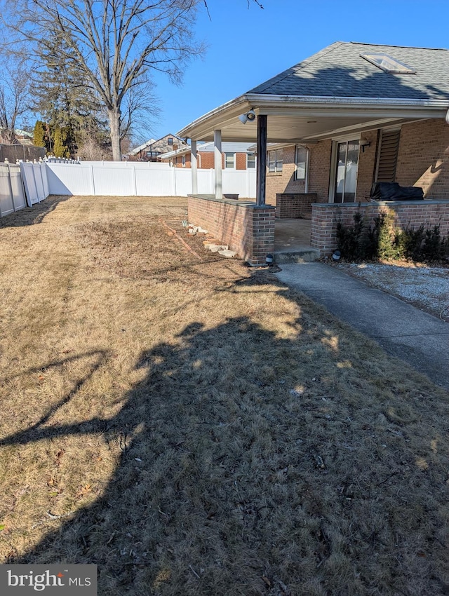 exterior space with a yard, brick siding, a shingled roof, and a fenced backyard