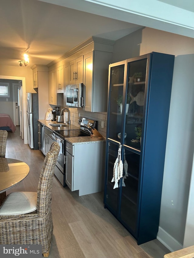 kitchen with stainless steel appliances, backsplash, white cabinets, a sink, and light wood-type flooring