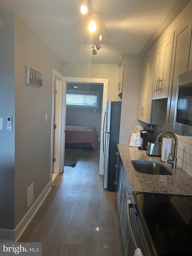 kitchen with stainless steel appliances, tasteful backsplash, dark wood-type flooring, a sink, and light stone countertops