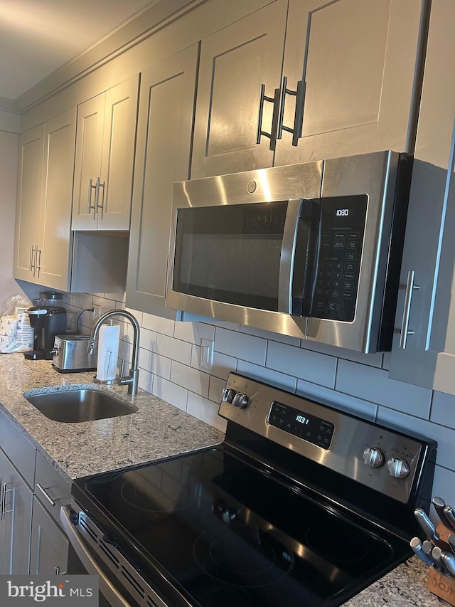 kitchen featuring decorative backsplash, light stone counters, appliances with stainless steel finishes, white cabinetry, and a sink