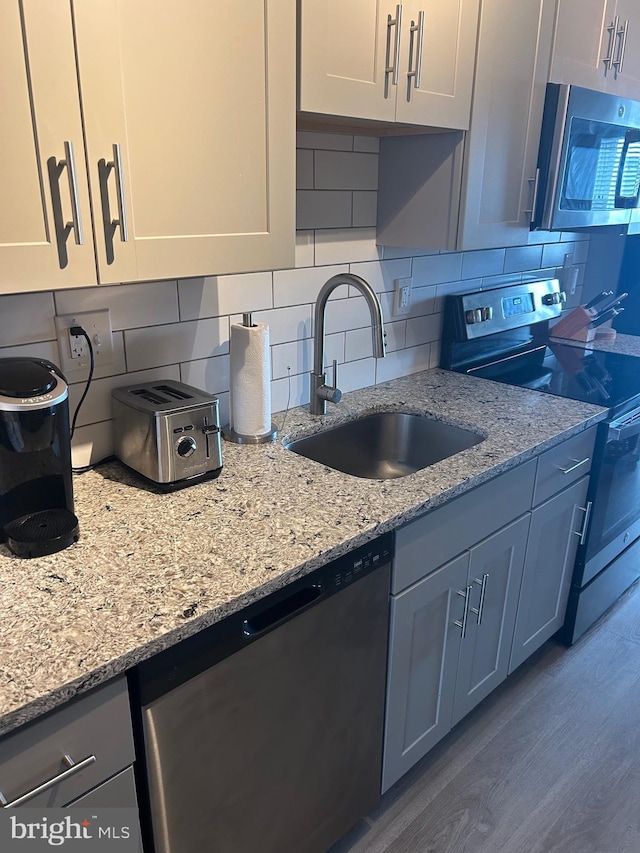 kitchen with appliances with stainless steel finishes, a sink, light stone countertops, and white cabinets