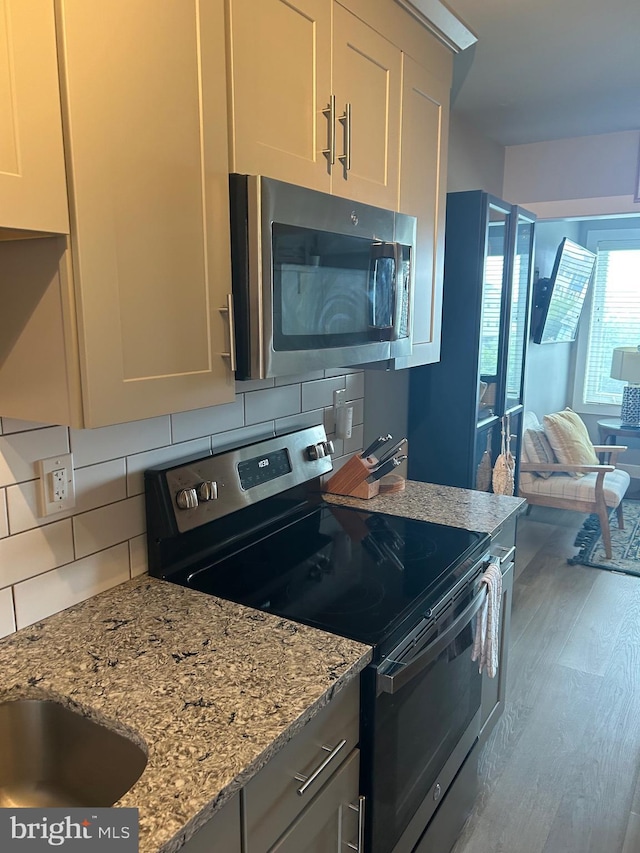 kitchen with decorative backsplash, appliances with stainless steel finishes, light stone counters, open floor plan, and light wood-style floors