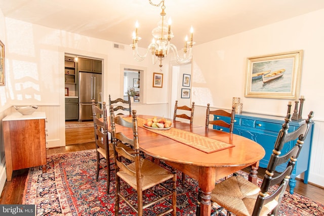 dining room featuring a chandelier, wainscoting, visible vents, and wood finished floors