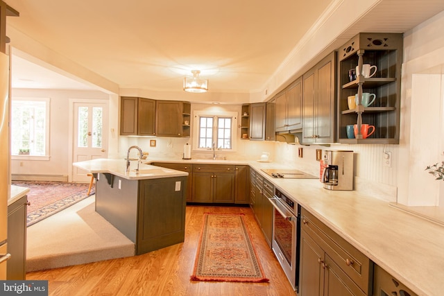 kitchen with open shelves, baseboard heating, light wood-style floors, a sink, and oven