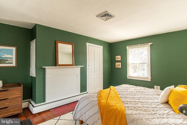 bedroom with a baseboard radiator, visible vents, and wood finished floors