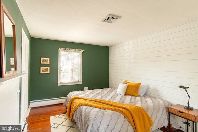 bedroom with baseboards, visible vents, baseboard heating, and wood finished floors