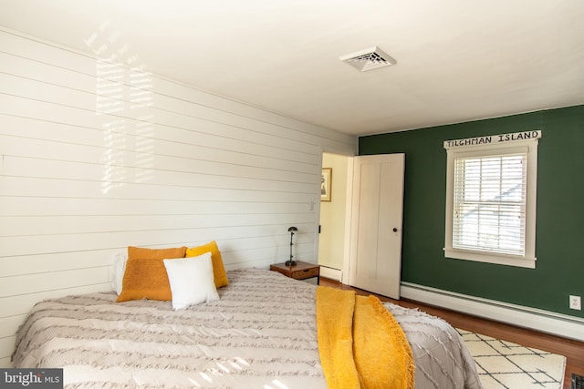 bedroom with a baseboard radiator, visible vents, a baseboard heating unit, and wood finished floors