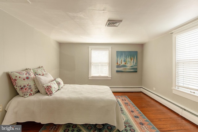 bedroom with a baseboard heating unit, visible vents, and wood finished floors