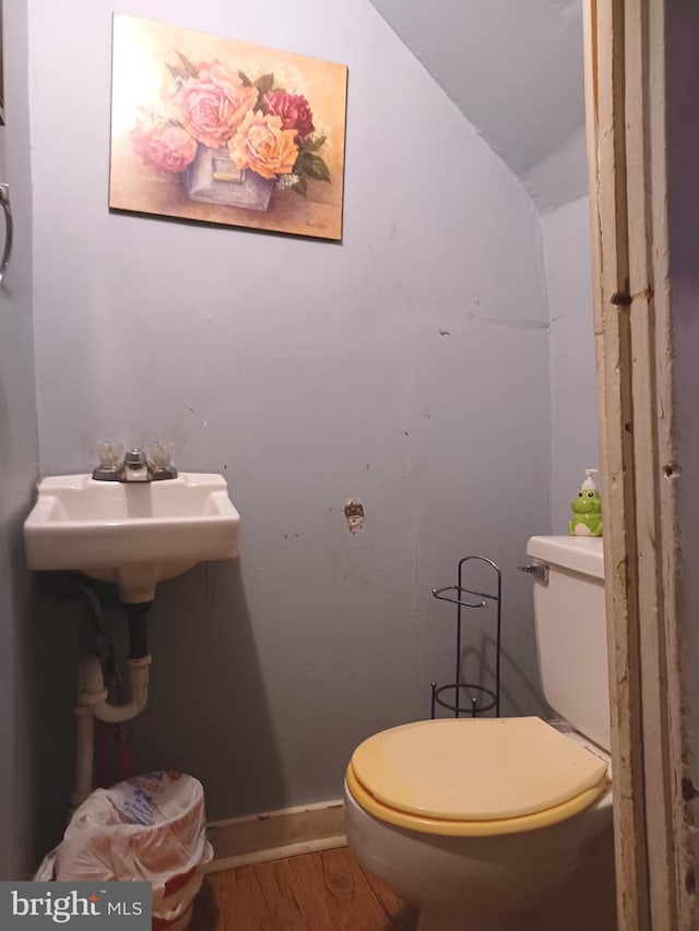 half bath featuring baseboards, toilet, lofted ceiling, wood finished floors, and a sink