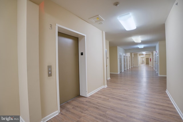 corridor featuring baseboards, light wood-type flooring, and elevator