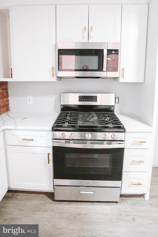 kitchen featuring appliances with stainless steel finishes, light wood-type flooring, white cabinetry, and light stone counters