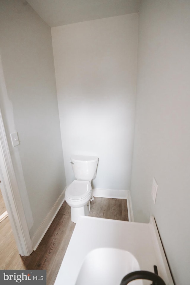 half bathroom with wood finished floors, toilet, and baseboards