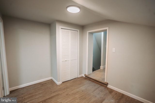 unfurnished bedroom featuring lofted ceiling, light wood finished floors, a closet, and baseboards