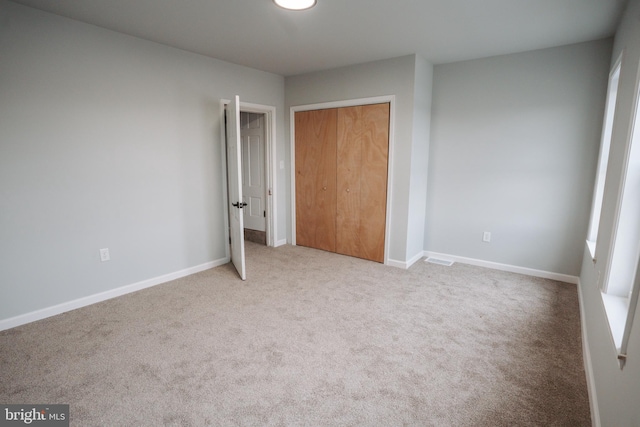 unfurnished bedroom featuring a closet, light colored carpet, and baseboards