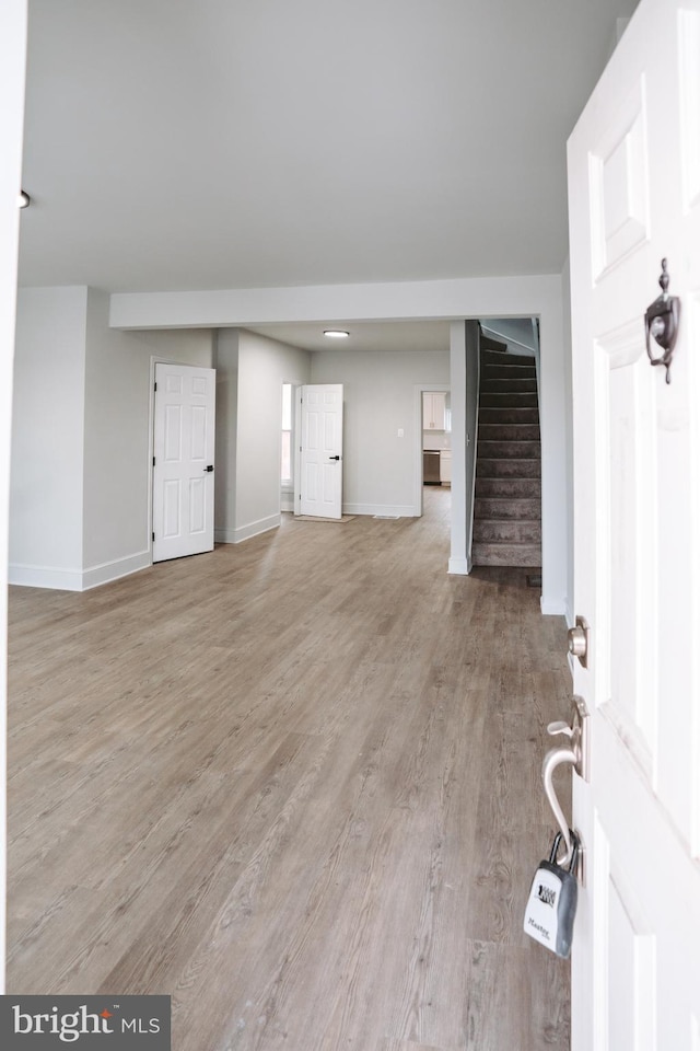 unfurnished living room featuring light wood-style flooring, stairs, and baseboards