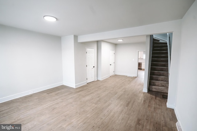 finished basement with baseboards, stairway, visible vents, and light wood-style floors