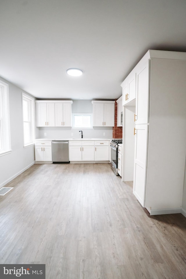 kitchen with appliances with stainless steel finishes, plenty of natural light, a sink, and white cabinetry