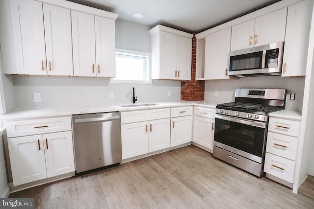 kitchen with stainless steel appliances, a sink, light wood-style flooring, and white cabinets