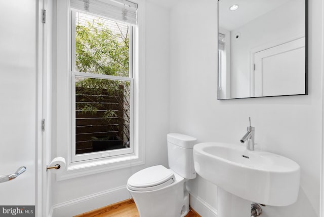 half bath with baseboards, a sink, toilet, and wood finished floors