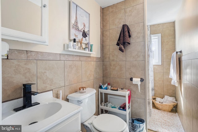 bathroom featuring toilet, tiled shower, vanity, and tile walls