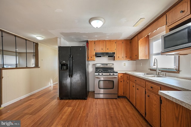 kitchen featuring under cabinet range hood, stainless steel appliances, a sink, light countertops, and brown cabinets