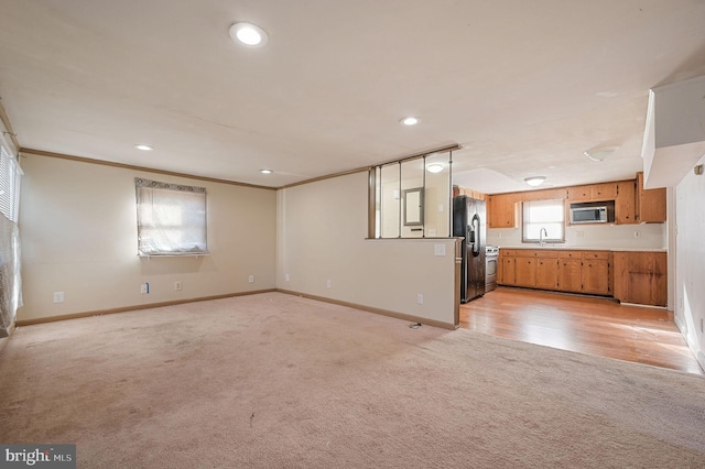 unfurnished living room with crown molding, light carpet, a sink, and baseboards