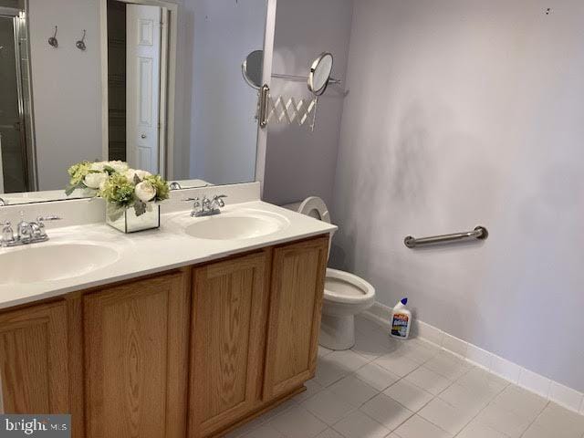 bathroom with double vanity, a sink, toilet, and baseboards