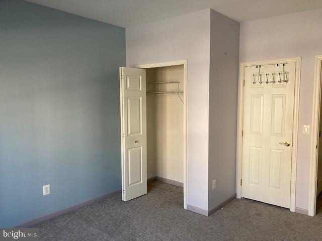 unfurnished bedroom with baseboards, dark colored carpet, and a closet