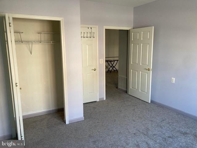 unfurnished bedroom with baseboards, dark carpet, and a closet