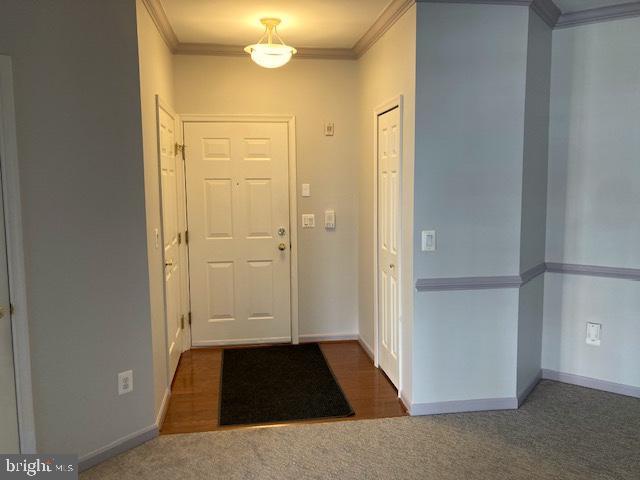 entryway with baseboards, ornamental molding, and dark carpet