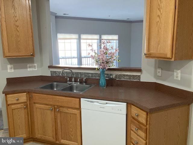 kitchen with brown cabinetry, dishwasher, dark countertops, ornamental molding, and a sink