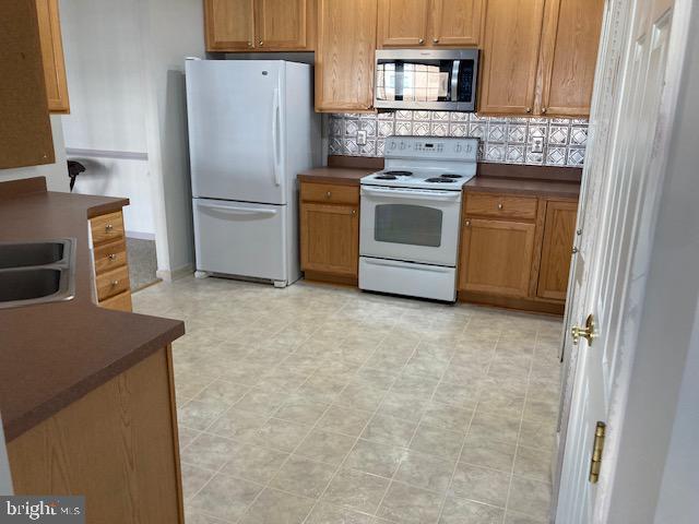 kitchen with dark countertops, white appliances, brown cabinets, and backsplash