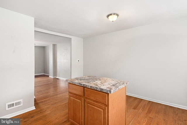 kitchen featuring a center island, visible vents, brown cabinetry, wood finished floors, and baseboards