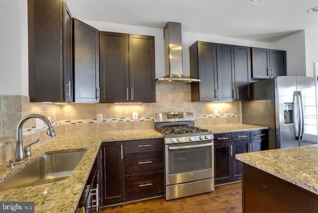 kitchen featuring light stone counters, stainless steel appliances, tasteful backsplash, a sink, and wall chimney exhaust hood