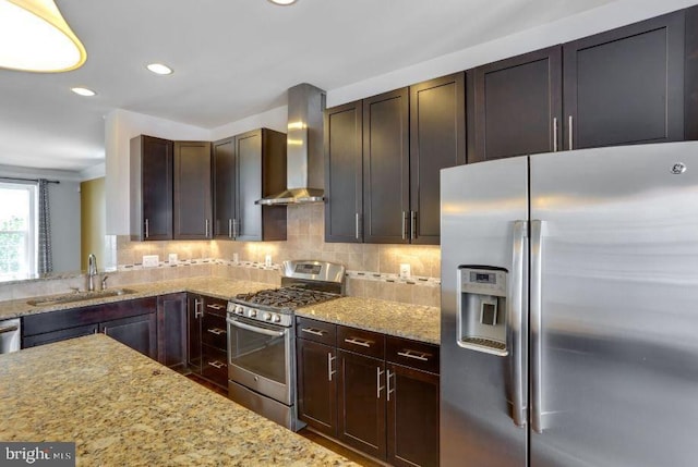 kitchen with stainless steel appliances, a sink, wall chimney range hood, and light stone counters